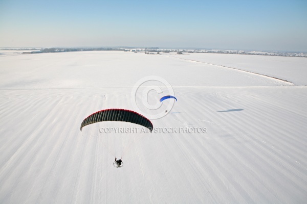 Paramoteur survolant un champ enneigé en hiver vu du ciel