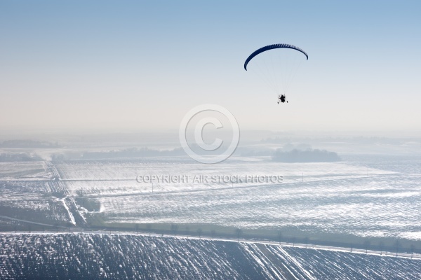 paramotor seen from the sky in France flying over snowy fields i