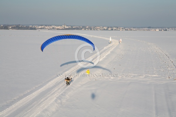 Parapente motorisé suivant une route enneigée avec un panneau